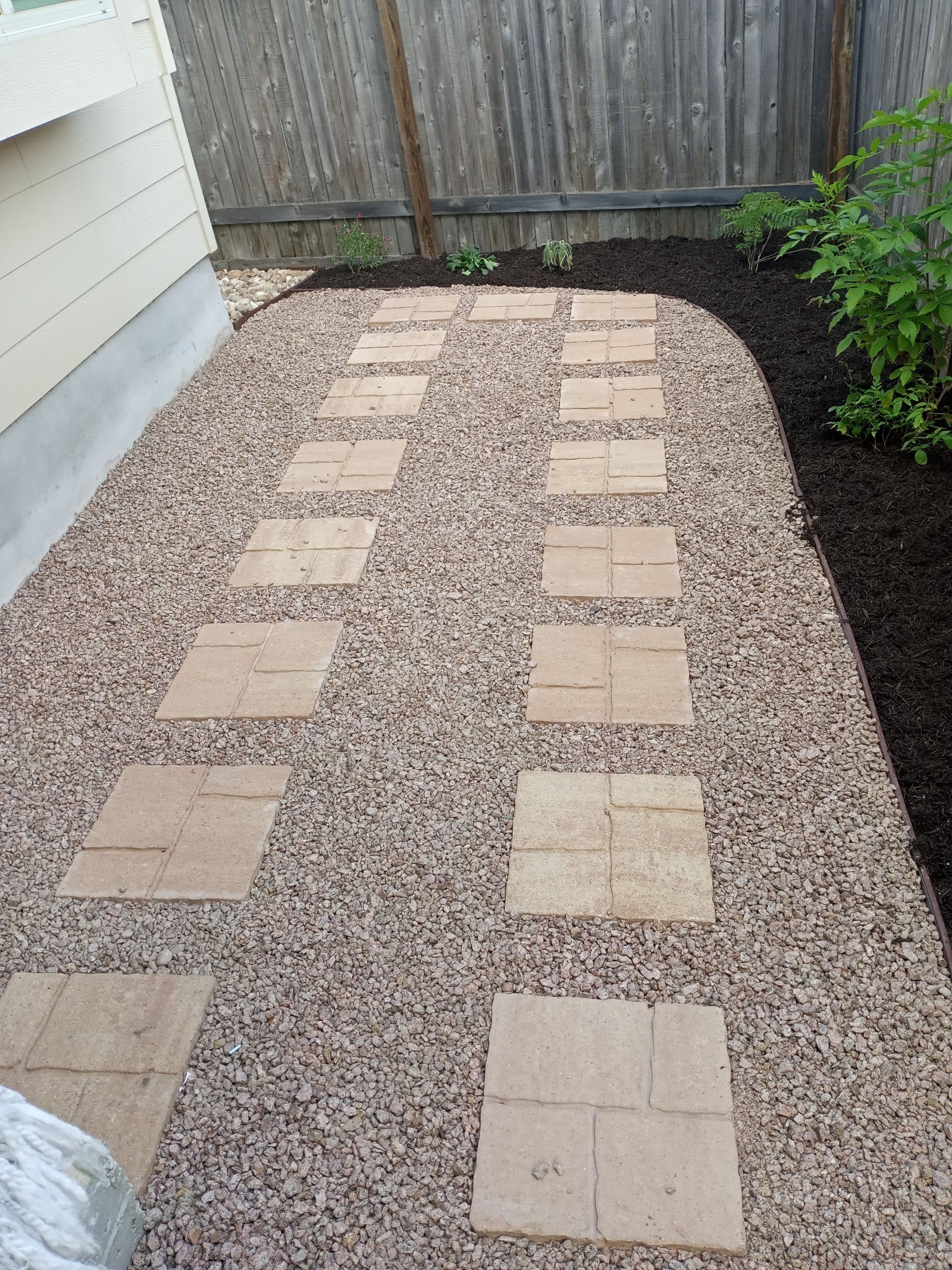 Stone pathway with stepping stones through gravel, beside a building and garden bed.