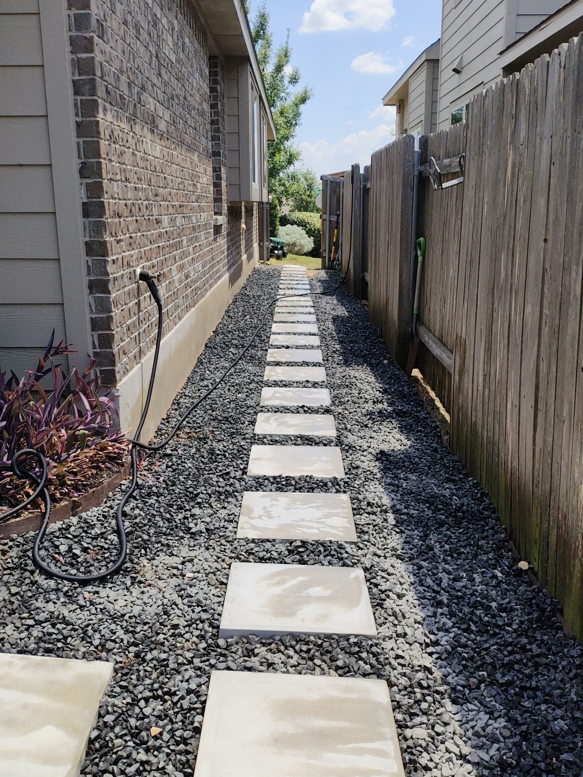 Stone path leads between a brick wall and a wooden fence, lined with gravel.