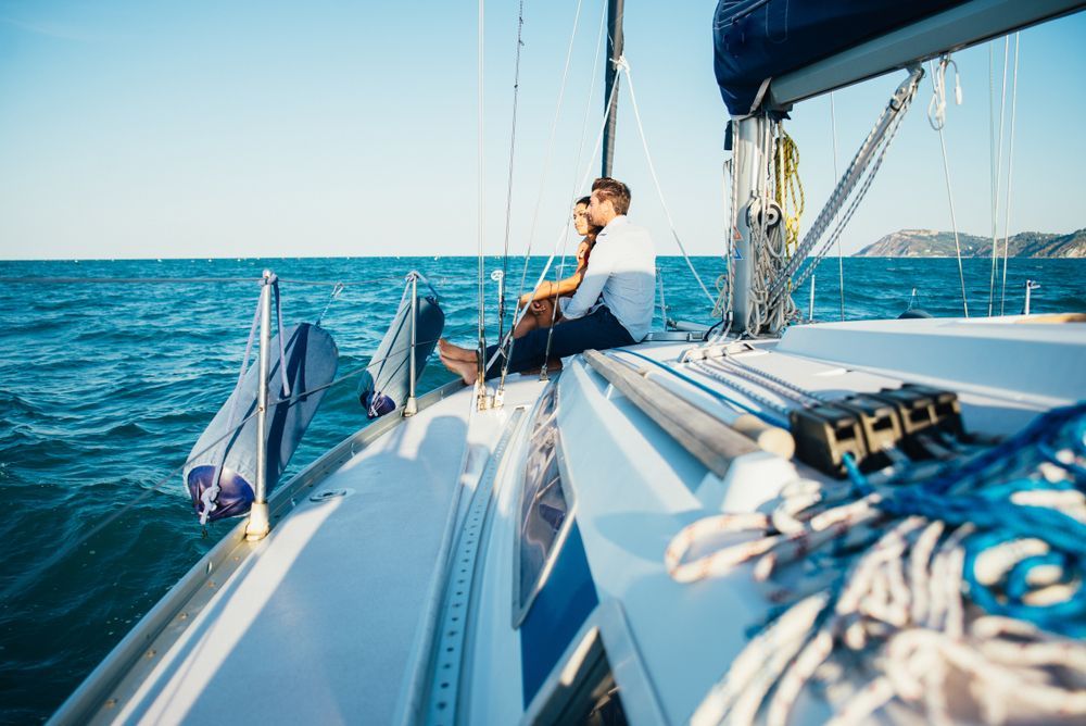 A couple is sitting on the deck of a sailboat in the ocean.