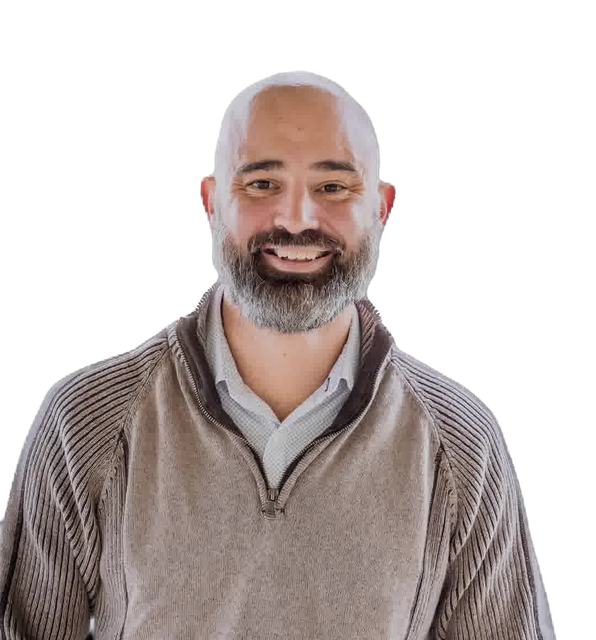Bald man with gray beard smiles, wearing a light-colored sweater over a collared shirt.