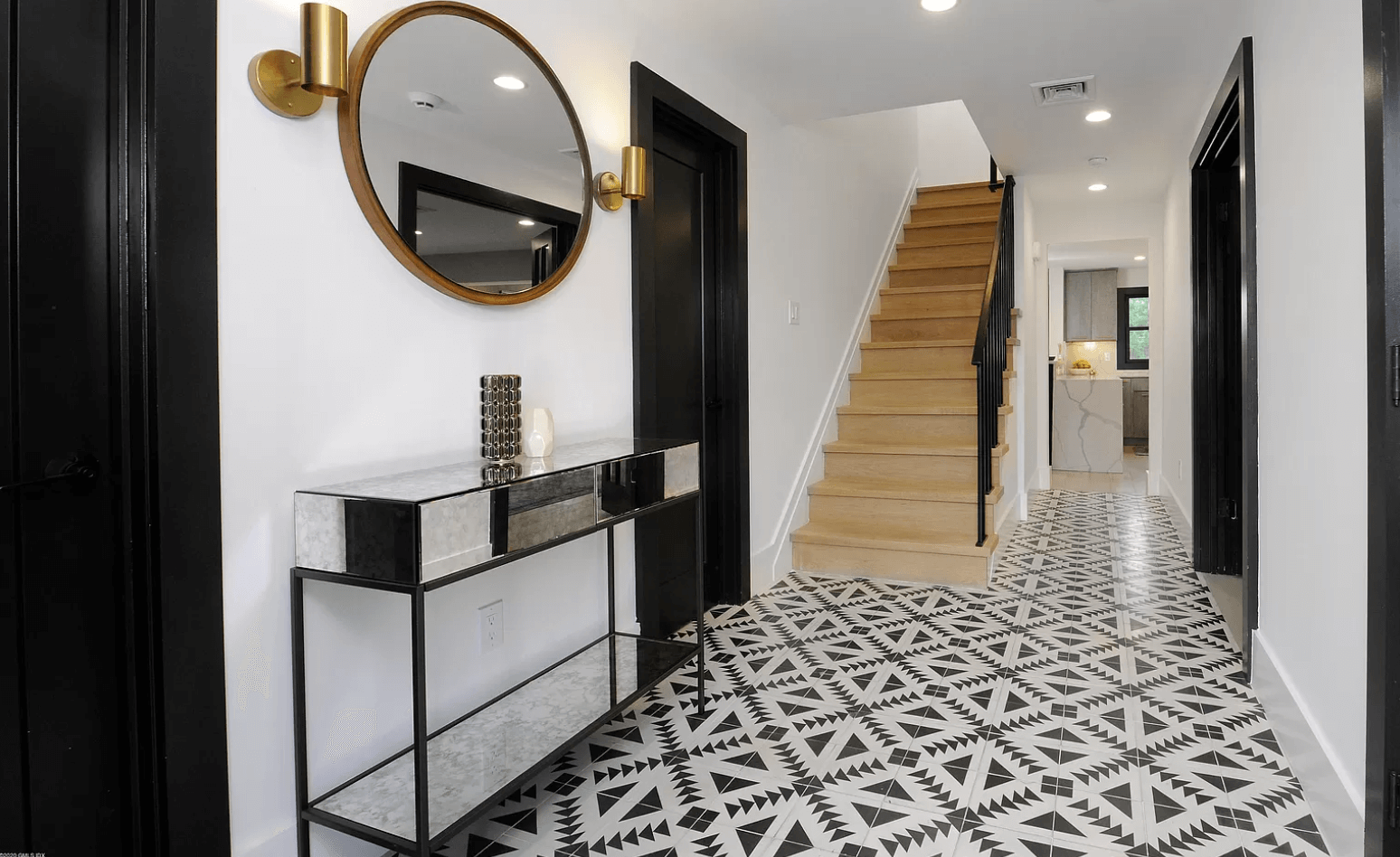 A hallway with a mirror , table , and stairs.