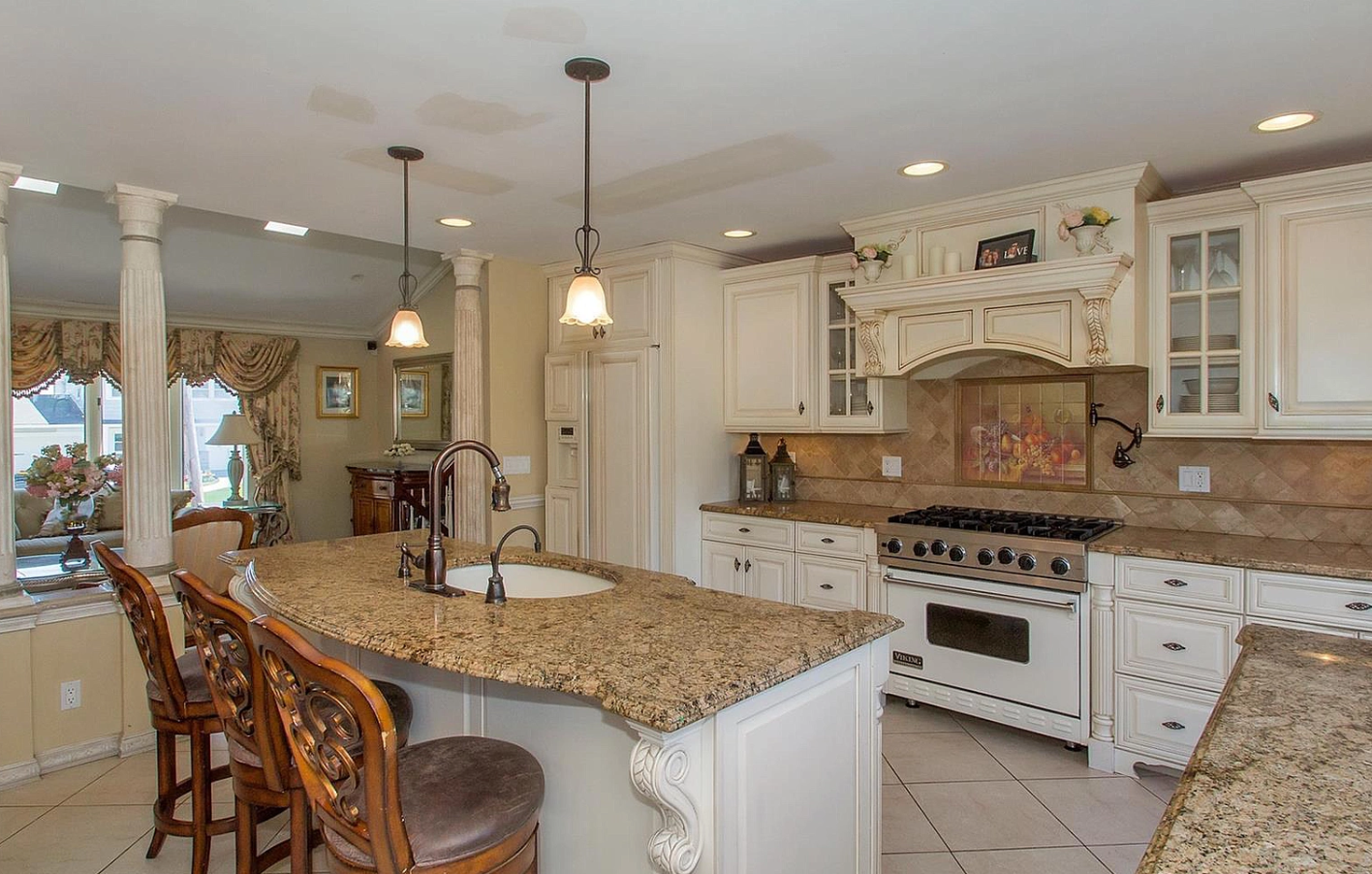 A kitchen with granite counter tops , white cabinets , a stove and a sink.
