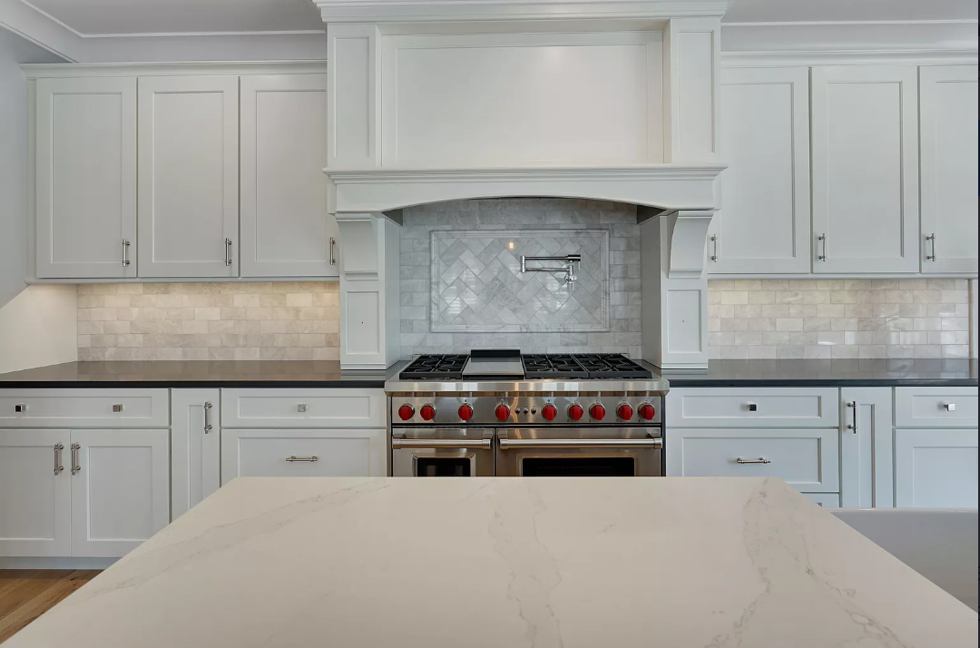 A kitchen with white cabinets , a stove , and a counter top.