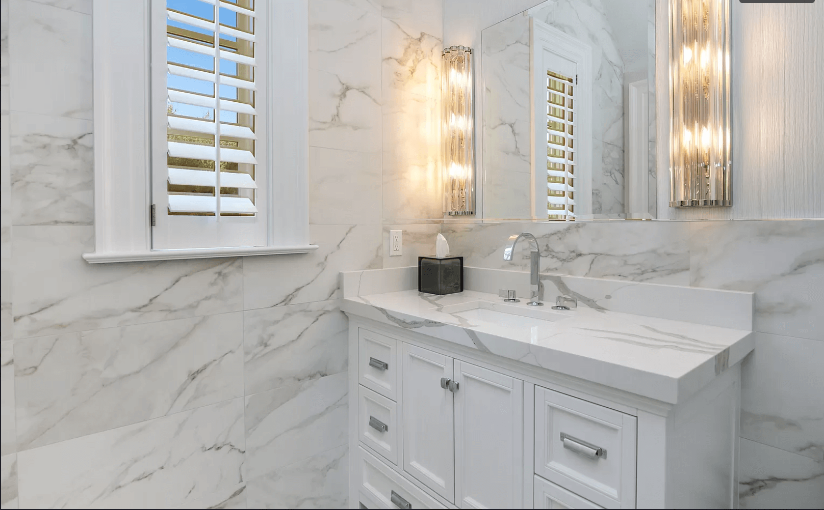 A bathroom with white cabinets , a sink , a mirror and a window.