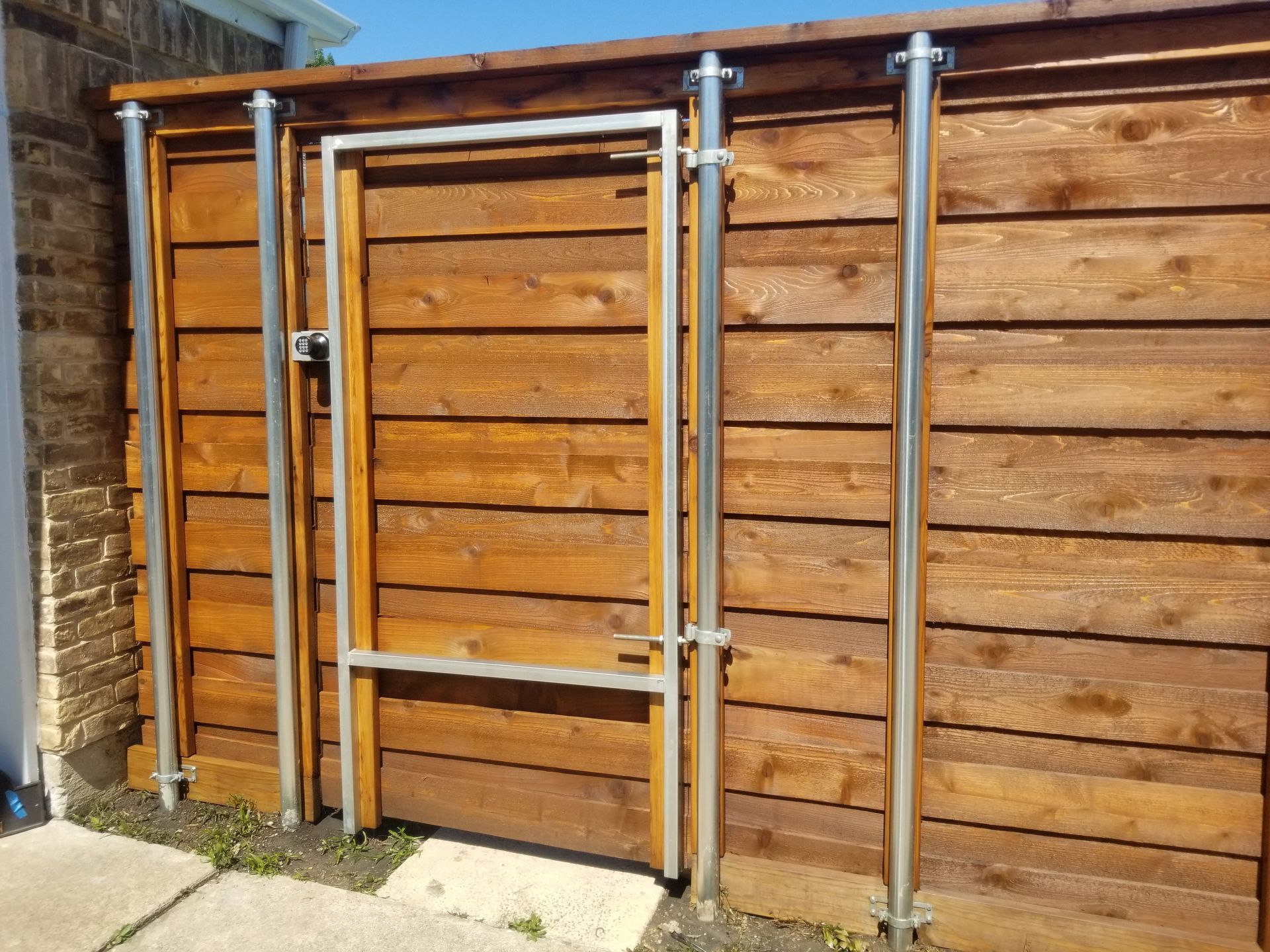 Closed metal gate set in a wooden fence beside a brick wall.