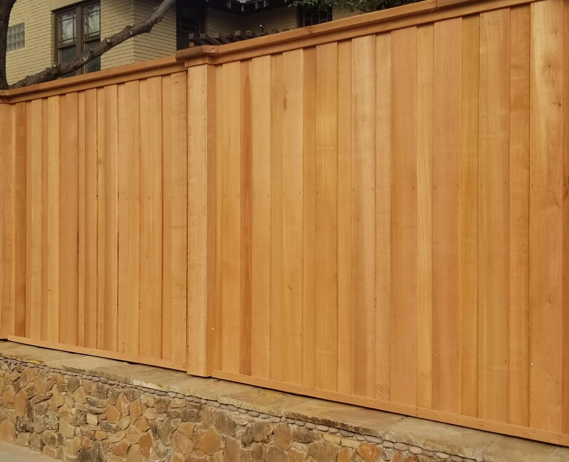 Wooden privacy fence with stone base beside a house