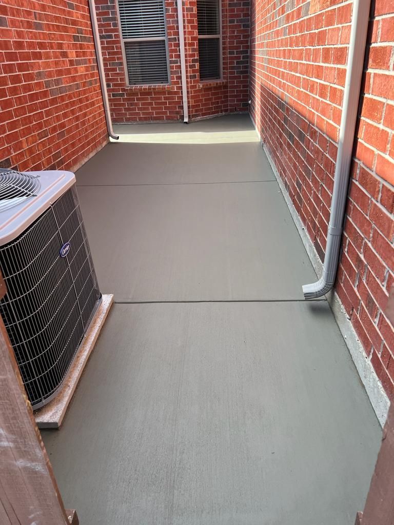Narrow brick-lined outdoor walkway with a gray concrete floor and an air conditioning unit on the left