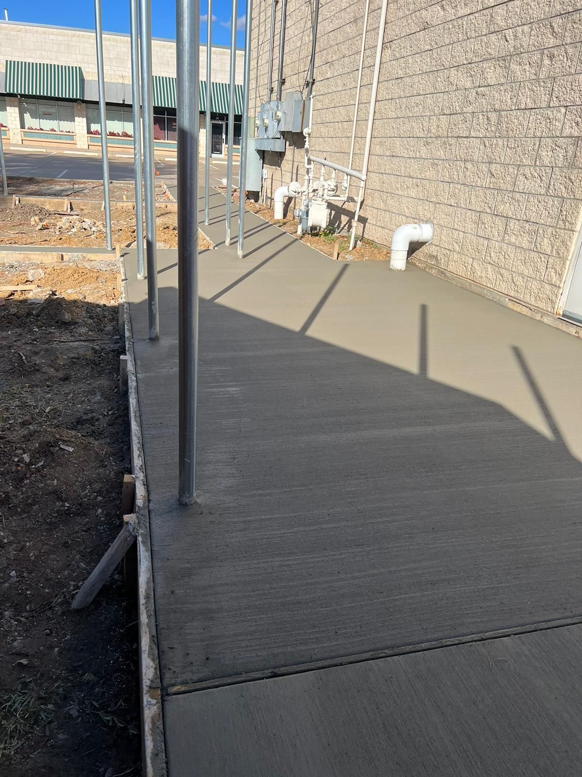 Freshly poured concrete walkway beside a stone wall, with construction materials and fencing nearby