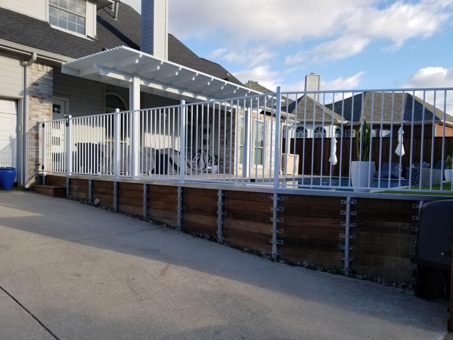 White-railed elevated deck beside a brick house, with stairs and a paved driveway under a partly cloudy sky.