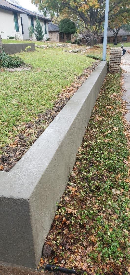 Long concrete retaining wall beside a grassy slope and sidewalk with fallen leaves.