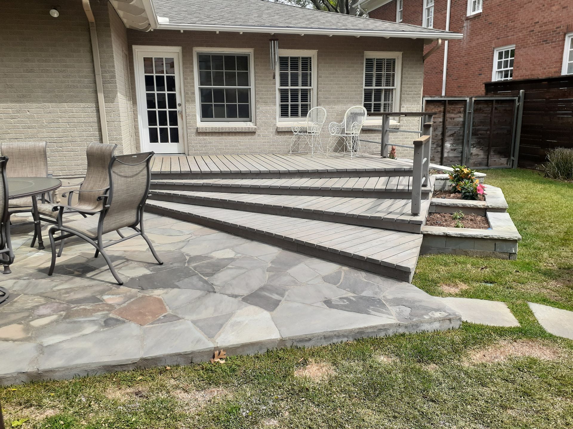 Backyard patio with stone steps, outdoor chairs, and planter beds beside a house