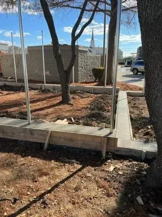 Concrete ramp beside a building, with trees, mulch, and a parked car in the background.