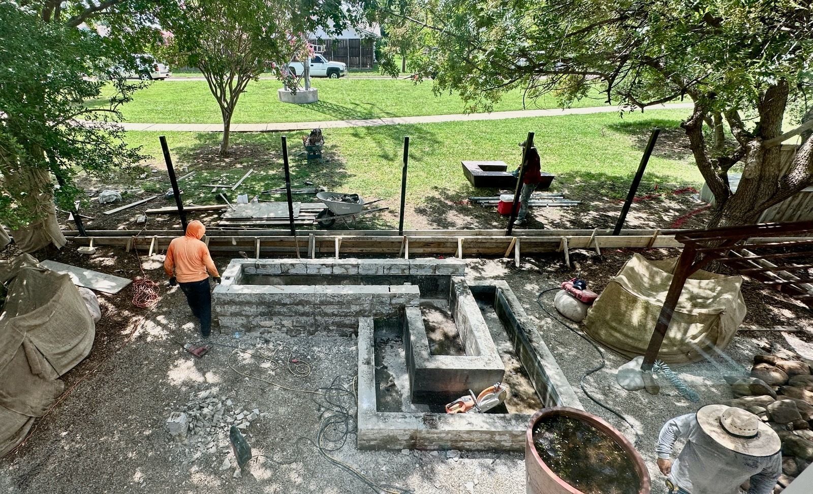 Person in orange shirt working at a concrete construction site beside a grassy park.