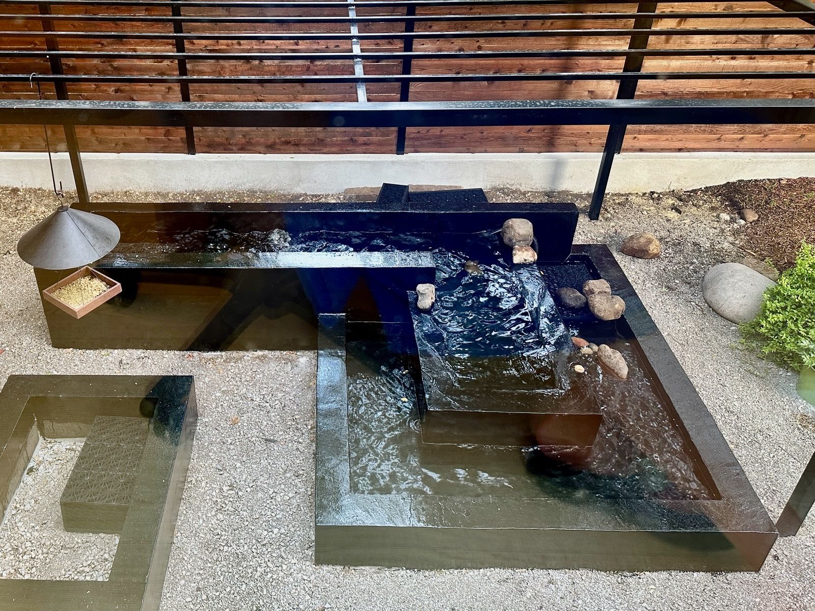 Small indoor water feature with stone basins, flowing water, and a wooden railing above