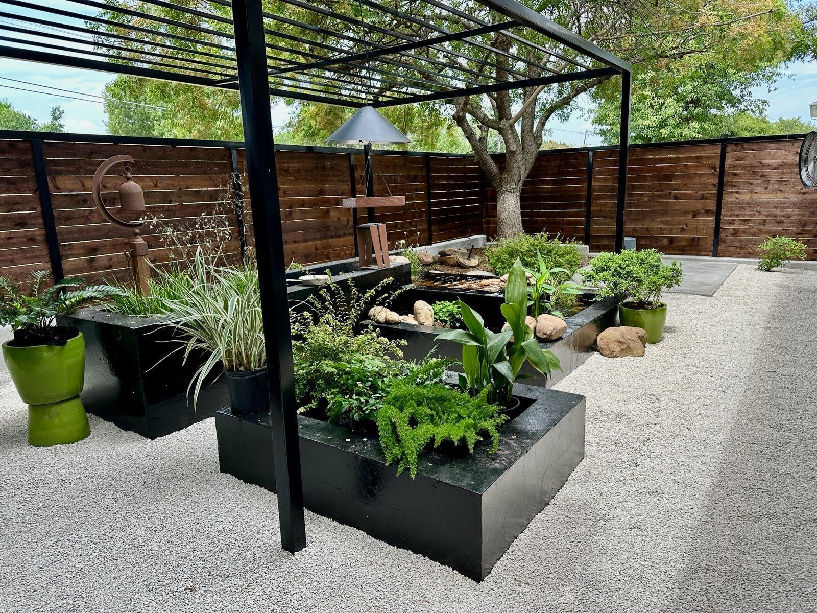 Modern backyard patio with raised planters, gravel ground, pergola frame, and wooden privacy fence
