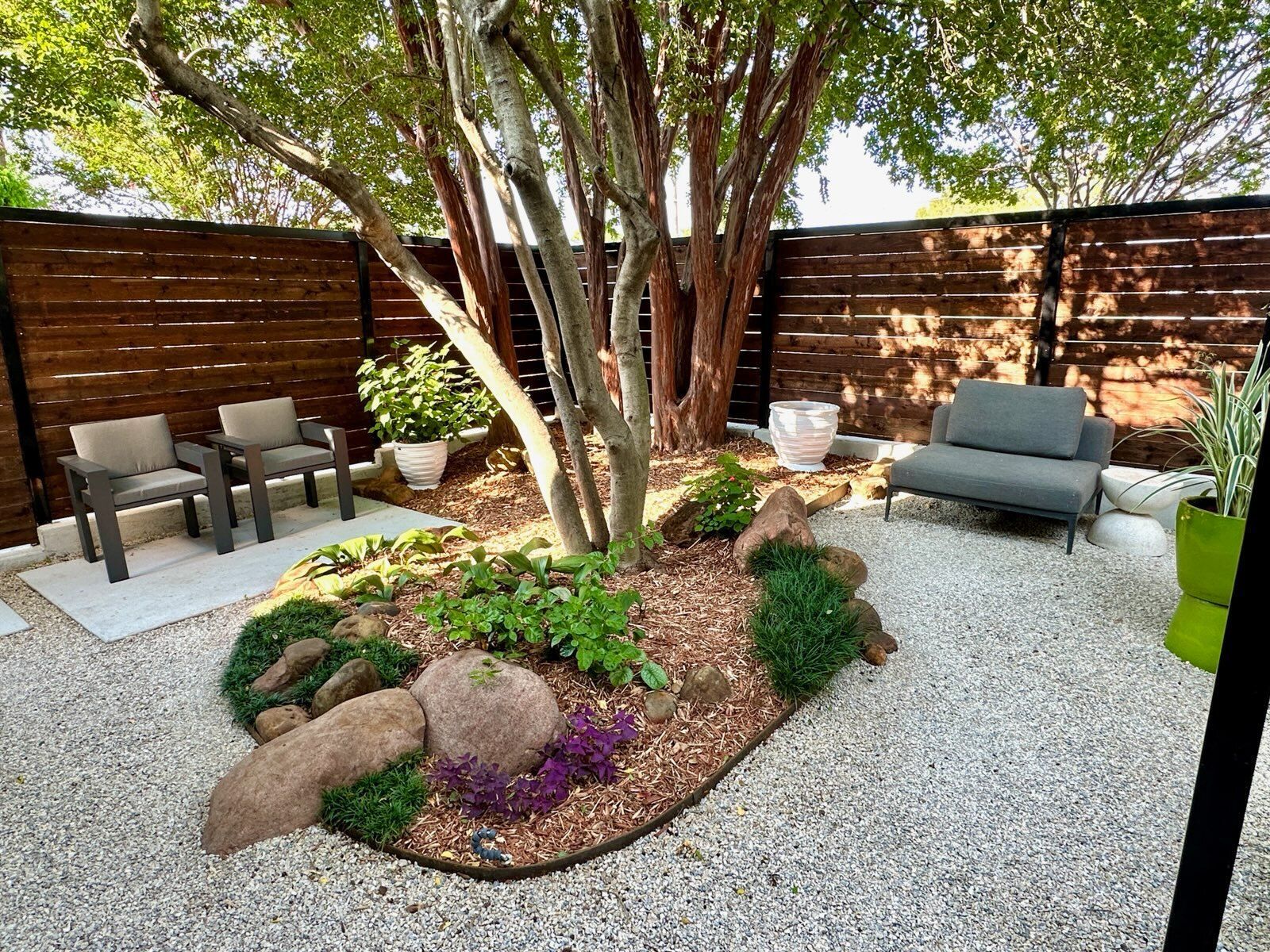 Wooded backyard patio with gravel, seating, and a landscaped tree island center