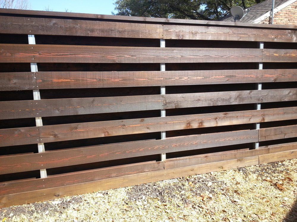 Brown wooden slat fence in a yard with sunlight and gravel ground below