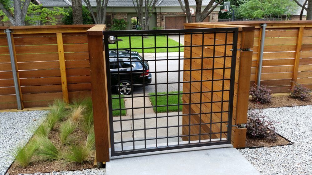 Wooden and black metal garden gate opening to a sidewalk and street, with a parked car beyond.