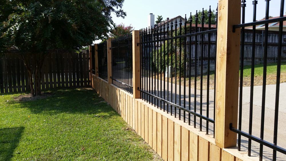 Wooden and black metal fence along a grassy roadside in bright daylight