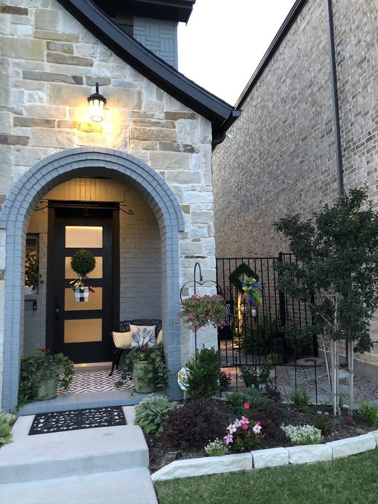 Stone house entry with arched doorway, lit porch lantern, and small landscaped garden path