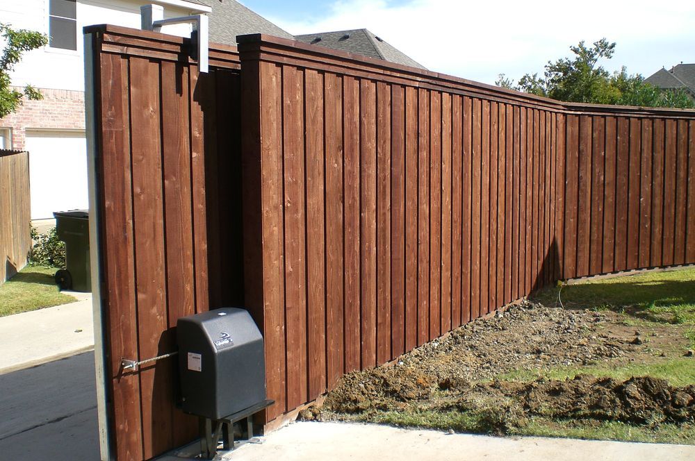 Brown wooden fence with a gate along a sidewalk beside a grassy yard and mailbox
