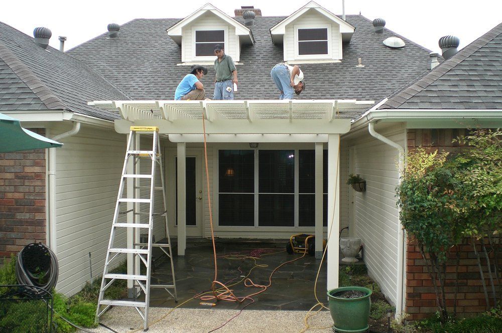 Two workers installing a white patio cover above a brick-and-siding house entrance