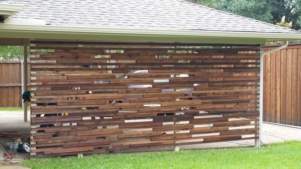 Wooden slatted privacy fence beside a grassy yard and driveway under a house roofline