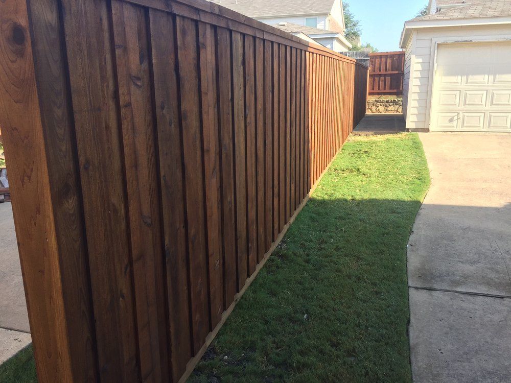 Wooden privacy fence beside a narrow grass strip and concrete driveway in a residential yard.