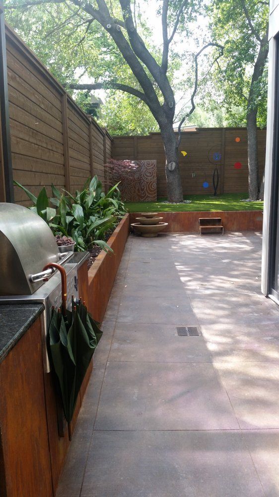 Wooden deck patio with grill, potted plants, and a large tree in the background.