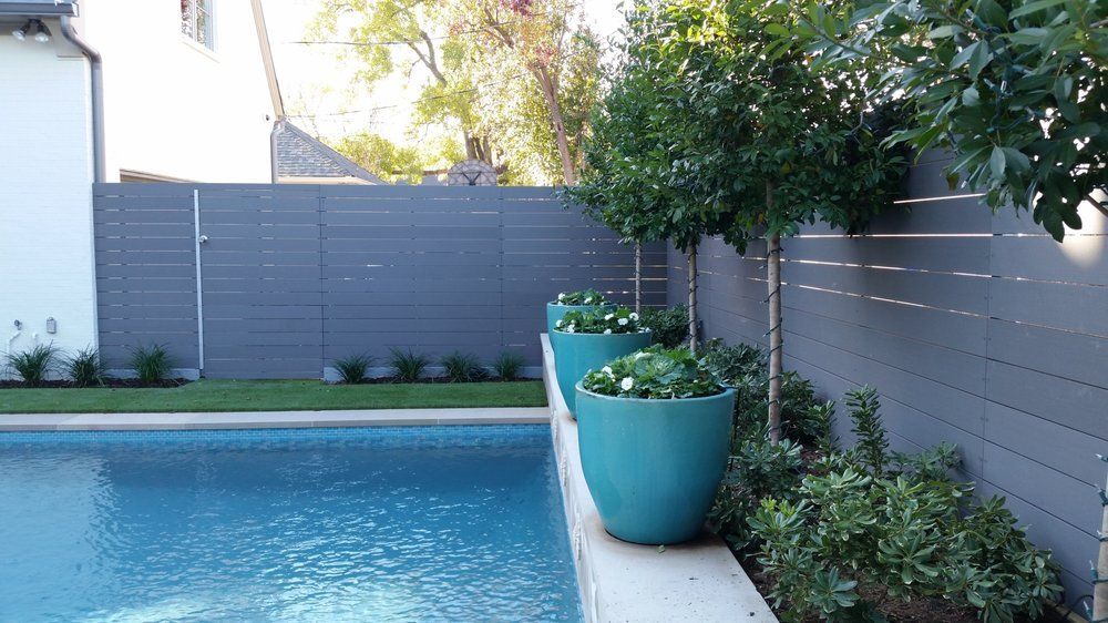 Backyard pool with blue water, gray fence, and large turquoise planters with greenery