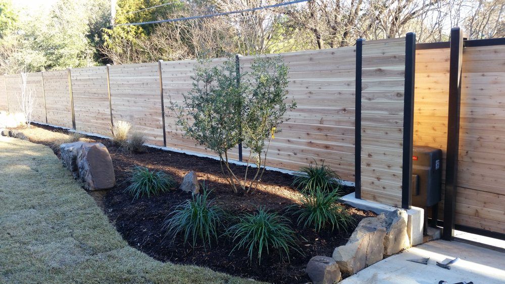 Modern landscaped yard with wooden fence, stone border, and small shrubs beside a gate
