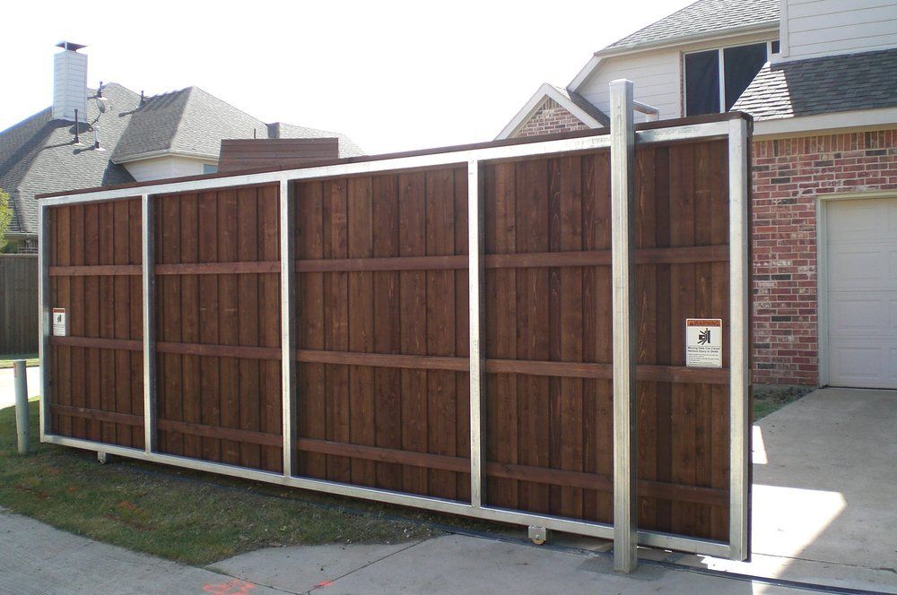 Wooden sliding driveway gate with white frame beside a house and garage