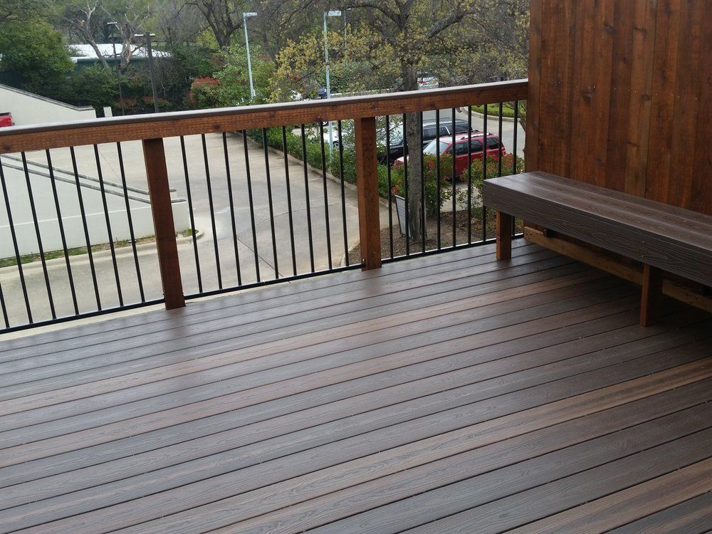 Wooden deck with railing and bench overlooking a driveway and trees