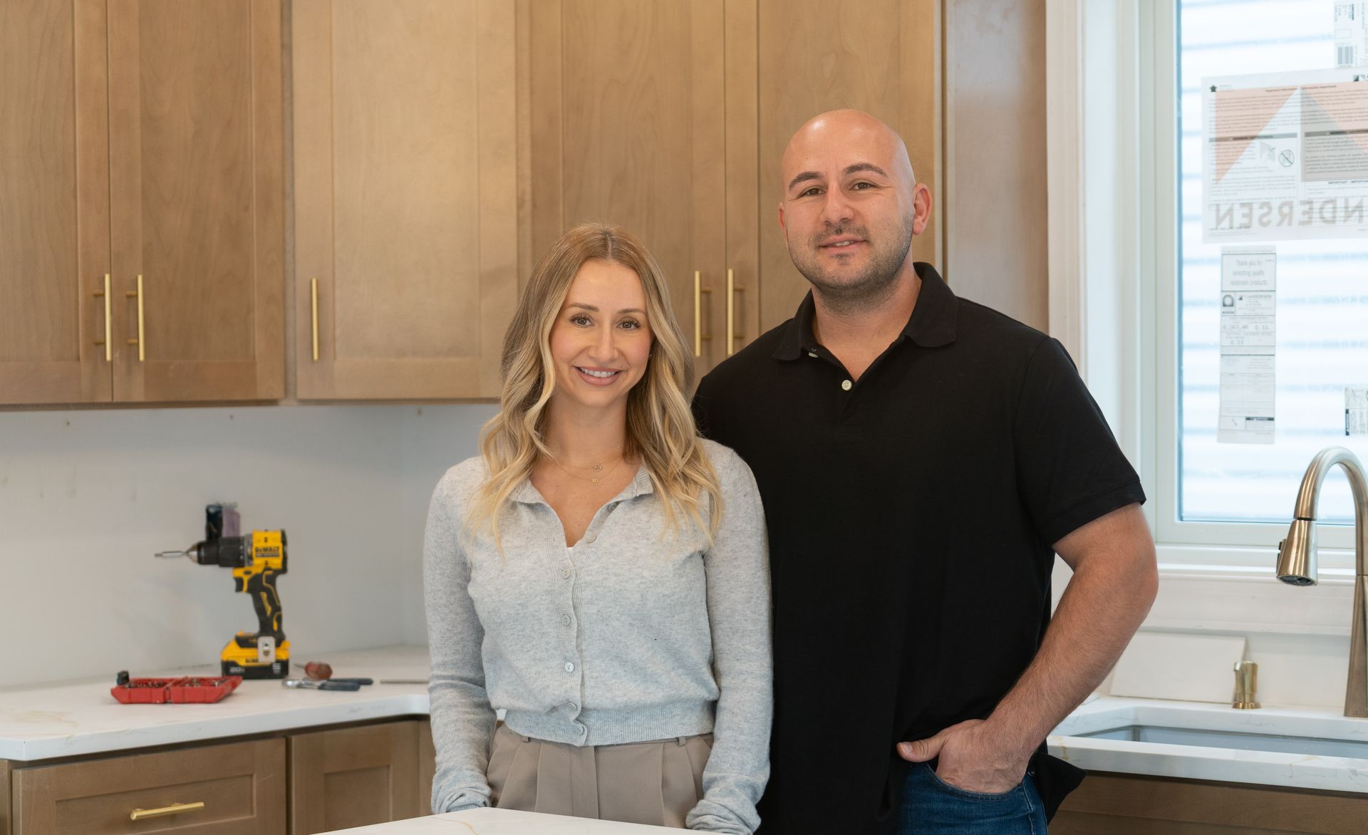 Two people standing in a bright kitchen beside white countertops and wood cabinets