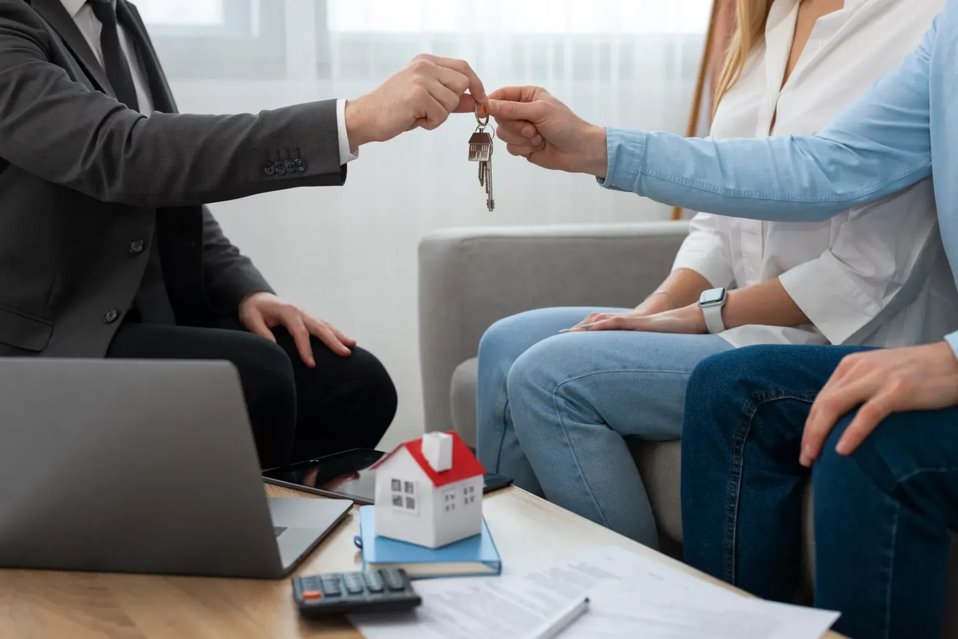 Agent handing house keys to seated clients during a home sale meeting