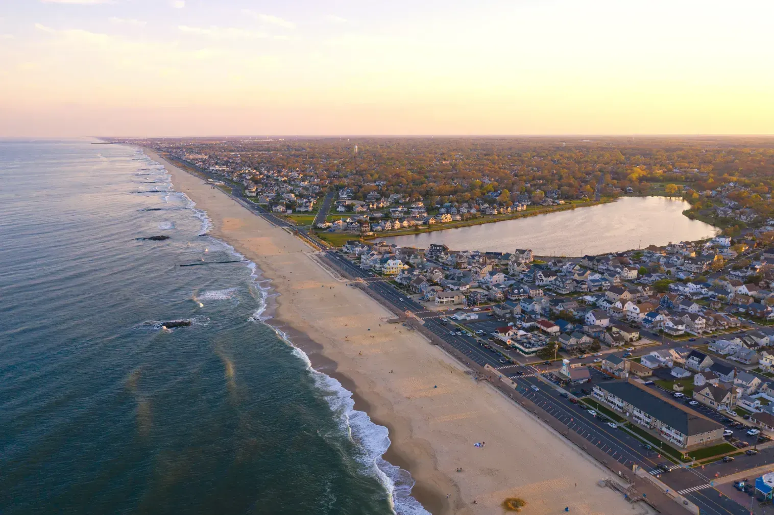 Aerial view of a coastline with beach, ocean waves, and a coastal town at sunset