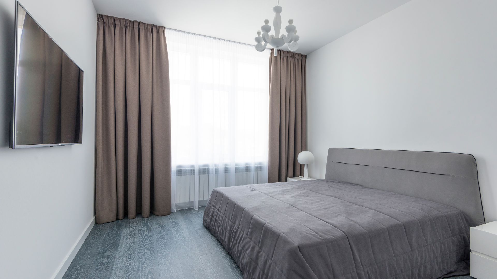 Bedroom with gray bed, brown curtains, and a chandelier.