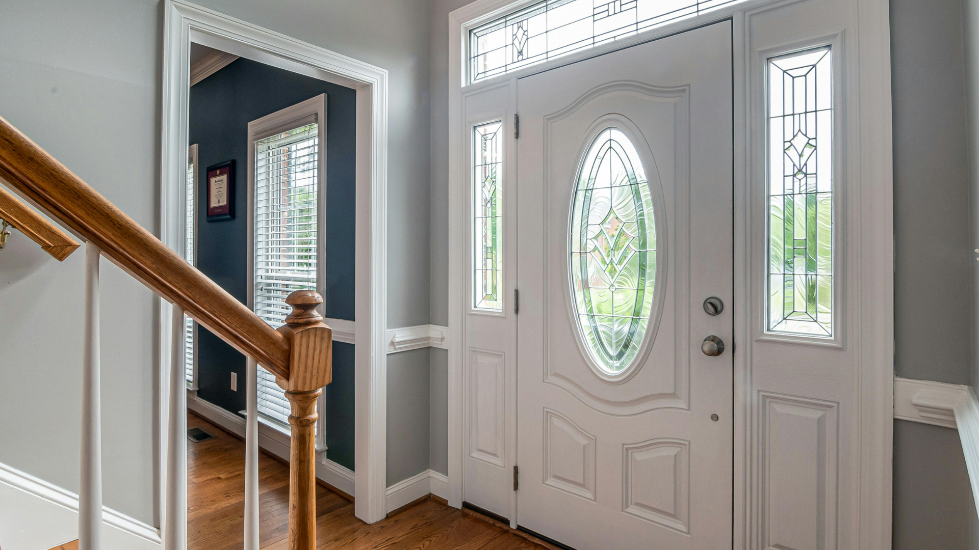White front door with oval glass and side panels, leading into a light gray entryway.