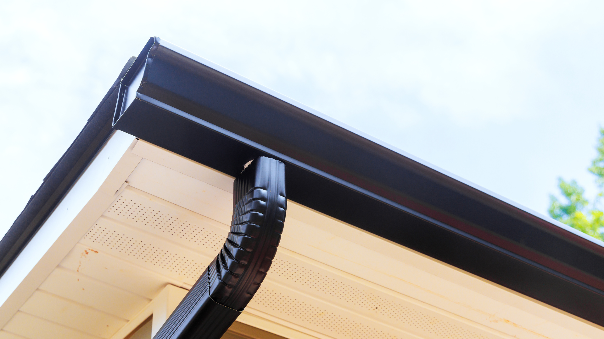 Black gutter on a beige soffit, angled shot with sky in background.
