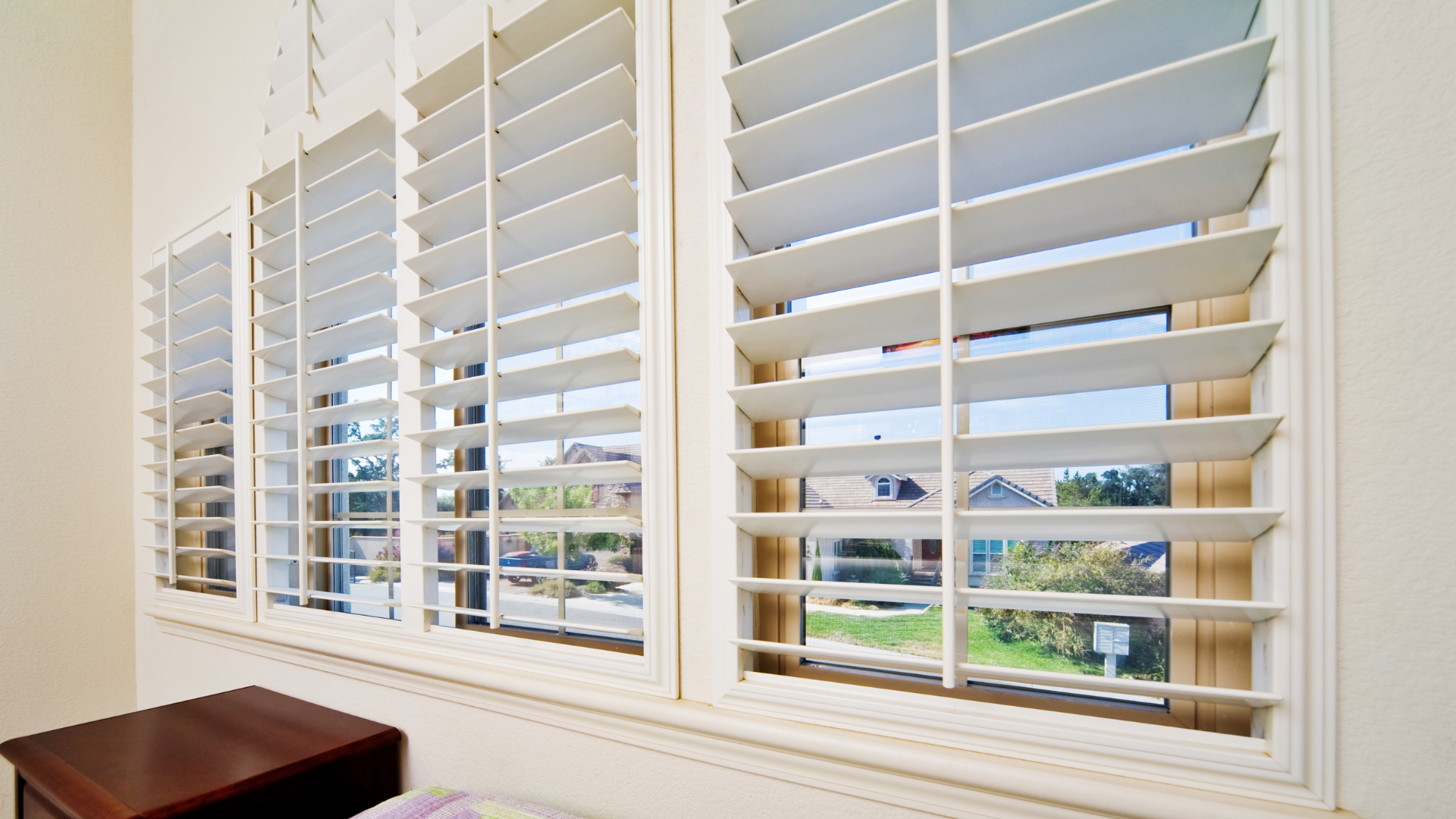 White plantation shutters on a window overlooking a sunny suburban street.