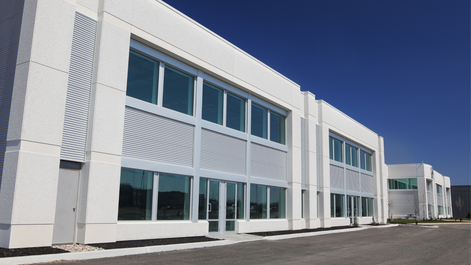 White modern commercial building with large windows under a clear blue sky.