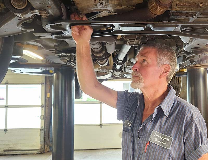 Mechanic working under a car raised on a lift. He uses a wrench  in the garage.