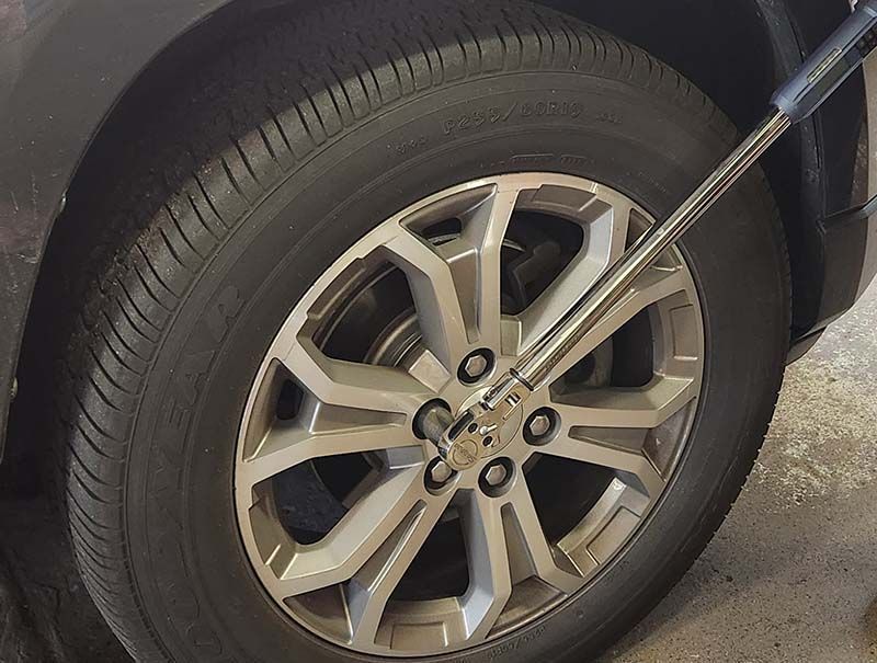 A car tire being worked on with a lug wrench. Hertzog's offers tires and alignment service.