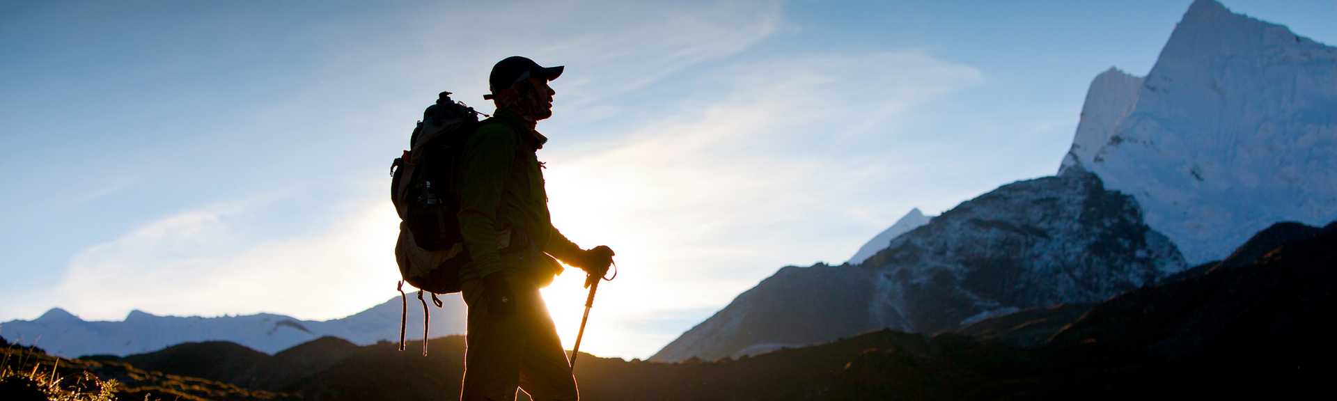 Silhouette of a hiker with backpack and walking stick at sunrise in the mountains