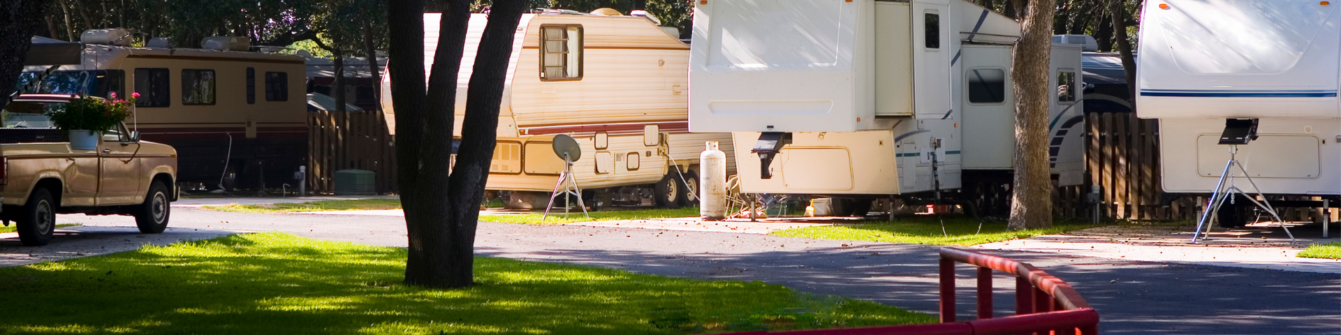 Row of RV trailers and a truck parked in a leafy campground beside a road