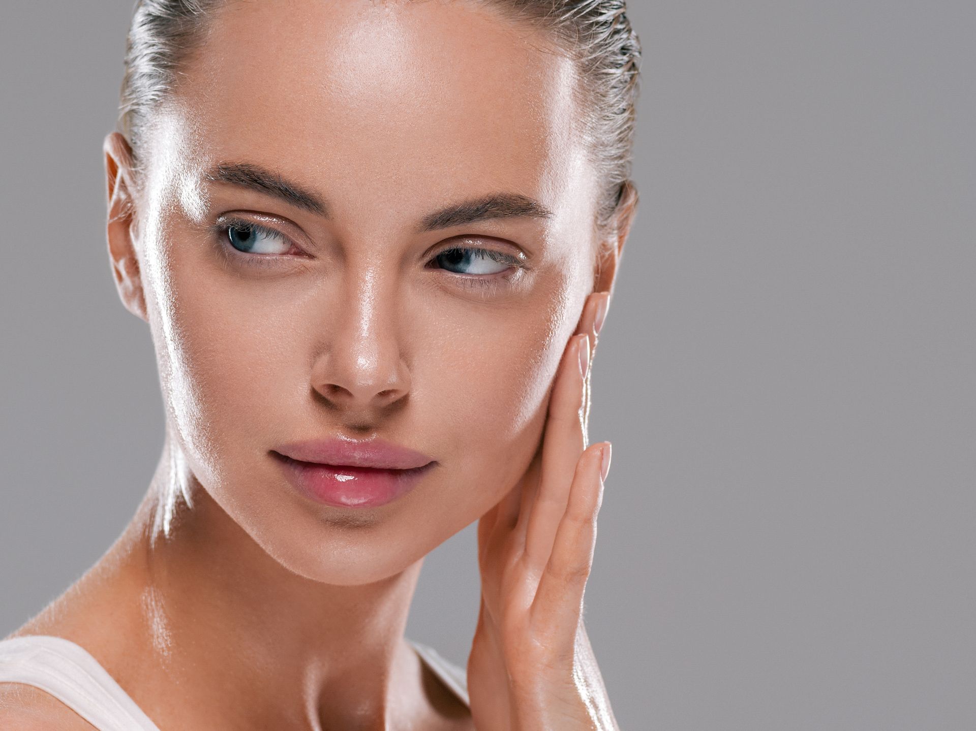 Une femme à la peau claire se touche le visage en regardant sur le côté. Fond clair.