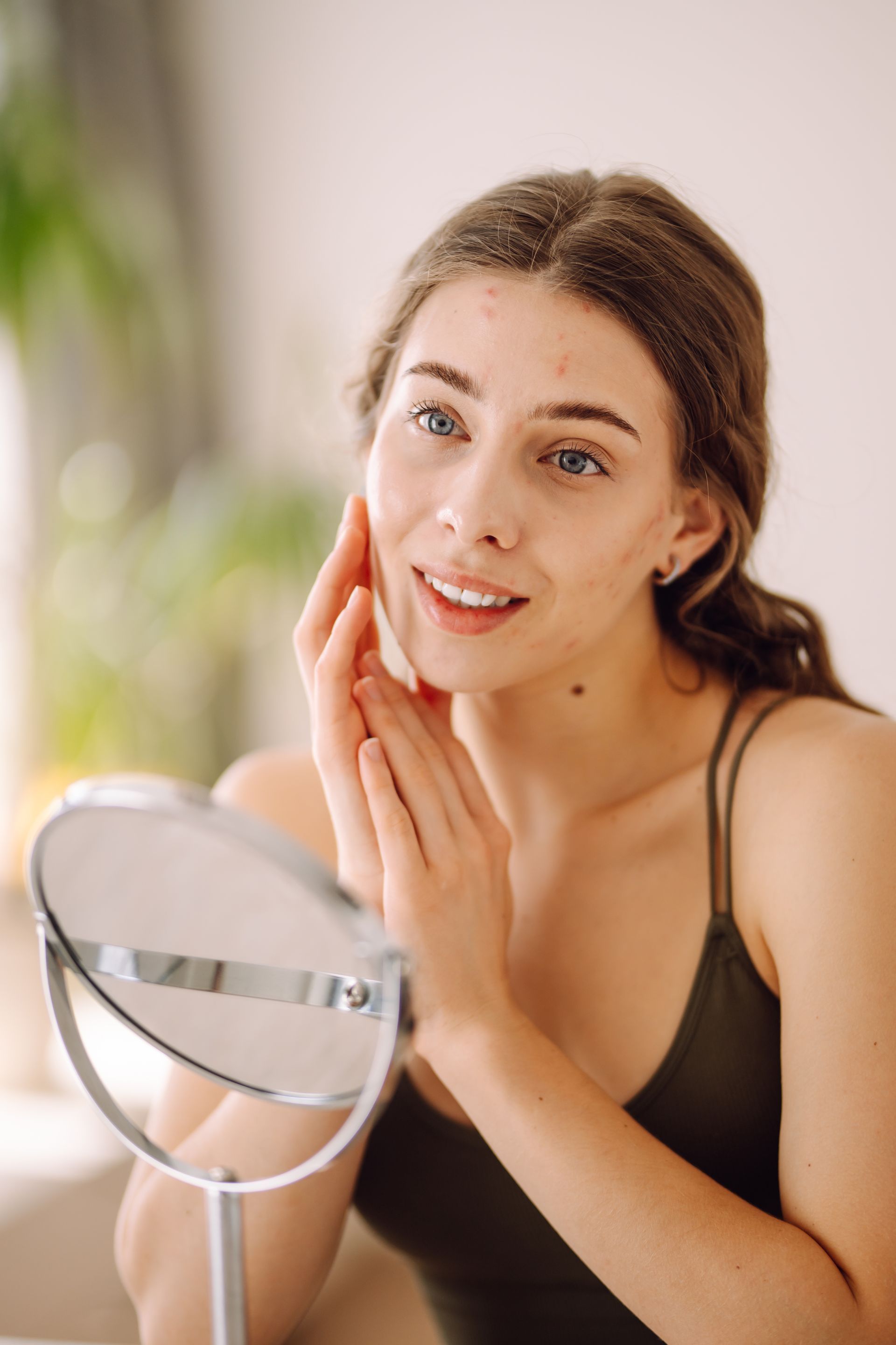 Femme se regardant dans un miroir, touchant son visage, petits boutons visibles, en intérieur.