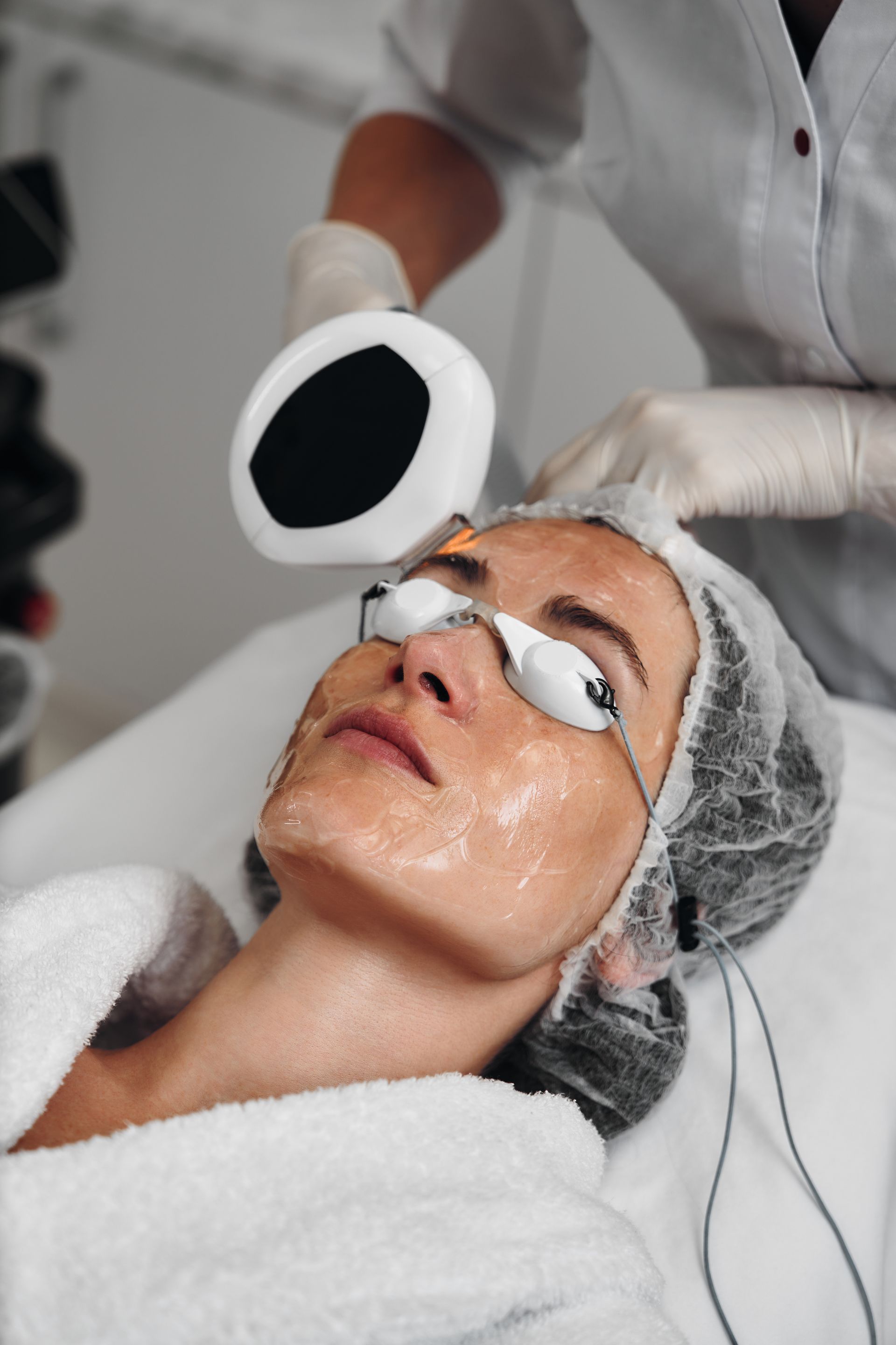 Femme recevant un soin du visage, portant des lunettes de protection, sous une lumière vive dans un spa.