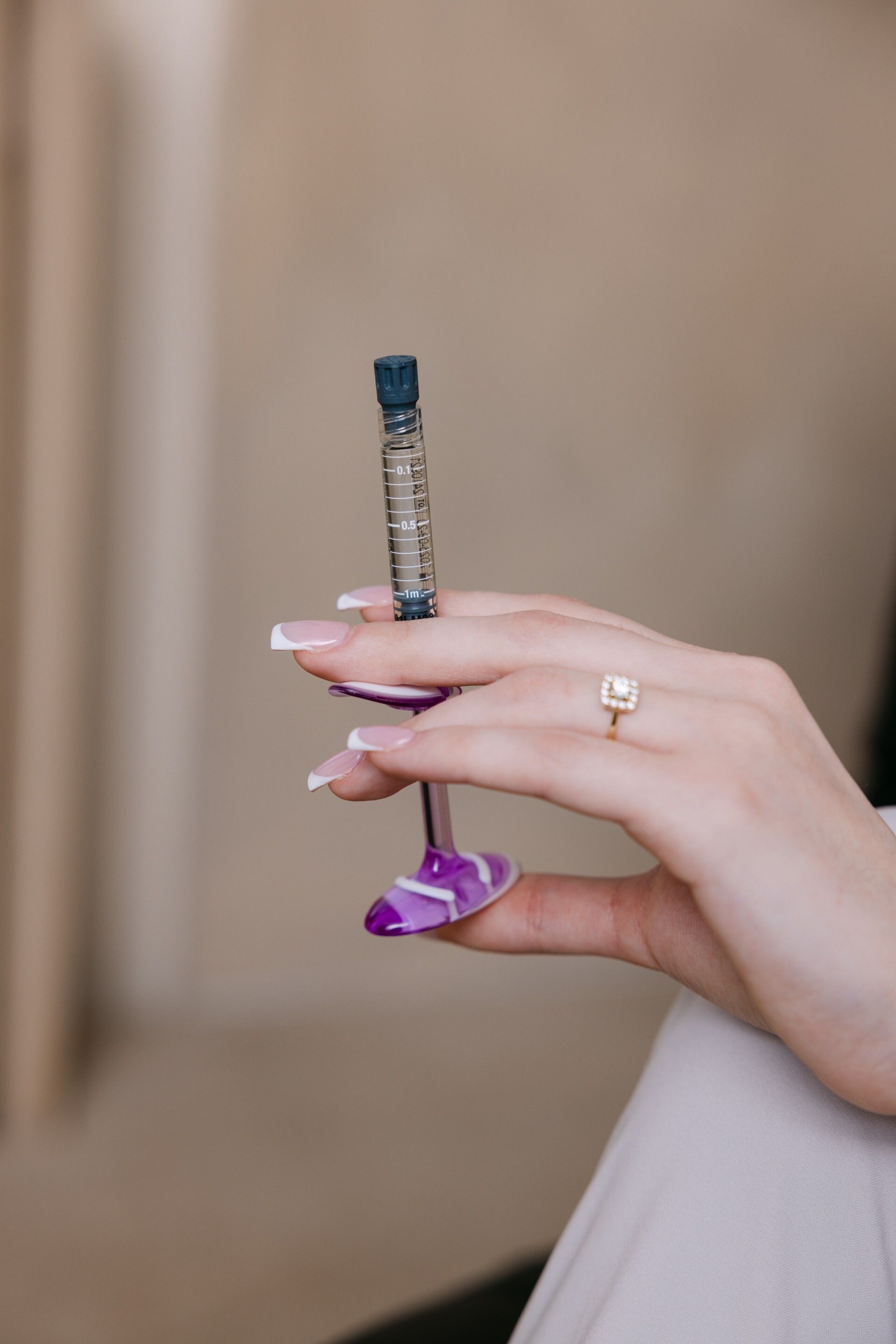 Person holding a prefilled injection with a purple handle and white and purple manicured nails.