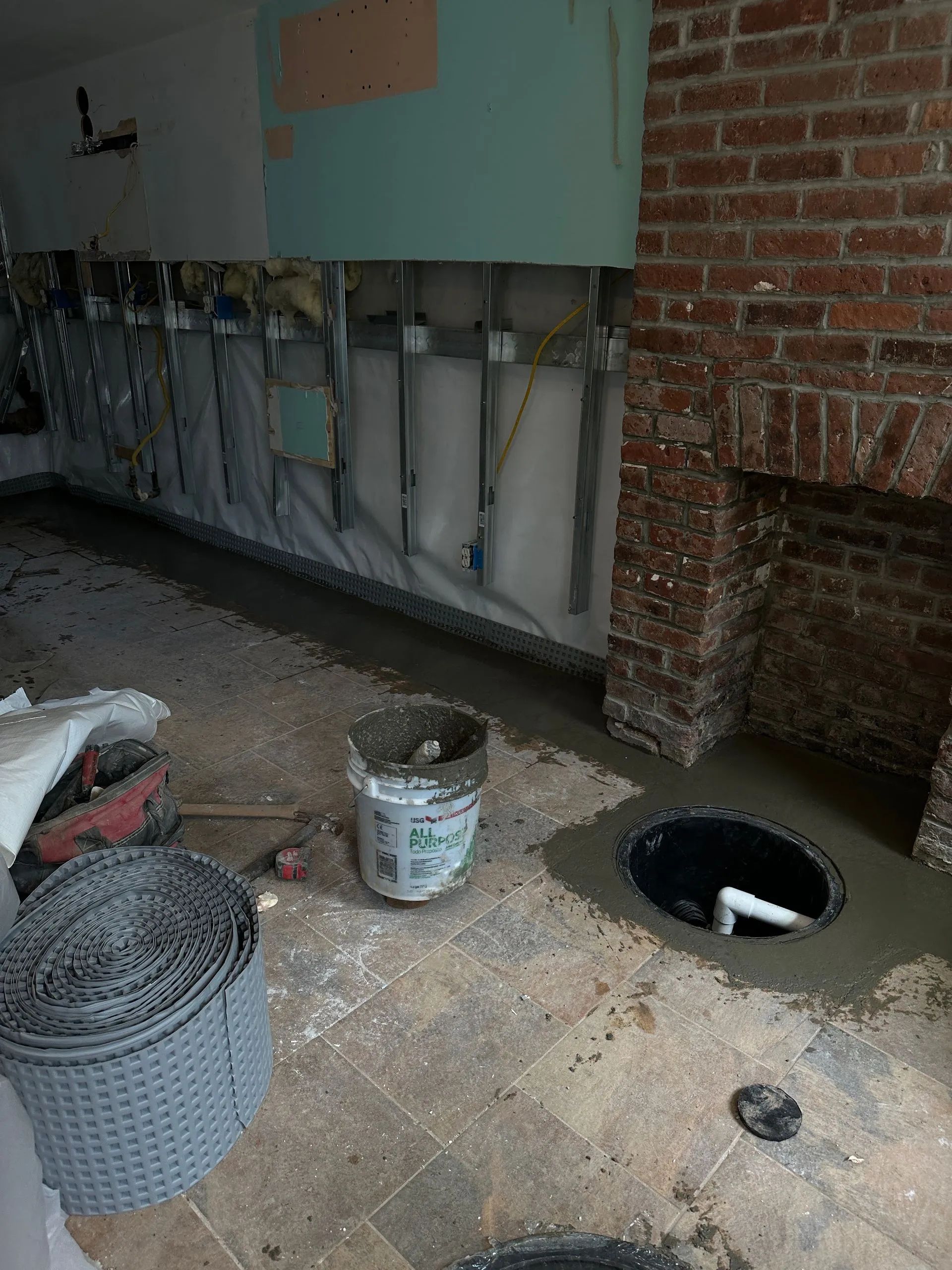 Basement renovation: concrete floor with a sump pump, drainage, and exposed brick and framing.